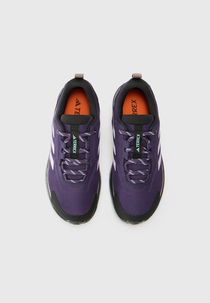 Zapatillas deportivas moradas con upper de malla, acentos negros y rayas blancas. Presentan cordones texturizados y una plantilla naranja. Diseño ligero.