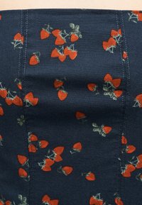 Ναυτικό ύφασμα με μικρές κόκκινες φράουλες και πράσινα φύλλα διασκορπισμένα, ορατή κάθετη ραφή στο ύφασμα.