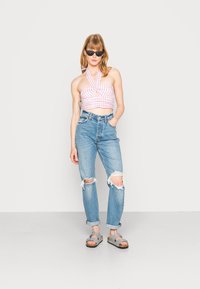 Top cropped em gingham rosa e branco com decote halter, combinado com jeans claros rasgados. Sandálias cinzentas com um detalhe em tira.
