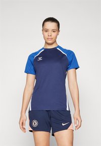 Navyblå atletisk T-shirt med korte ærmer og hvide accenter, parret med navy shorts med Chelsea FC-logo og lyserøde detaljer.