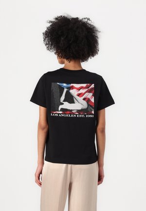 Sort t-shirt med et grafisk print af en hånd og det amerikanske flag på ryggen, med teksten "LOS ANGELES EST. 1981" nedenfor. Korte ærmer.