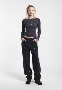 Top lungo a maniche nere a coste con cuciture blu a contrasto, abbinato a jeans in denim scuro a gamba larga con dettagli a pressione e tasche laterali.