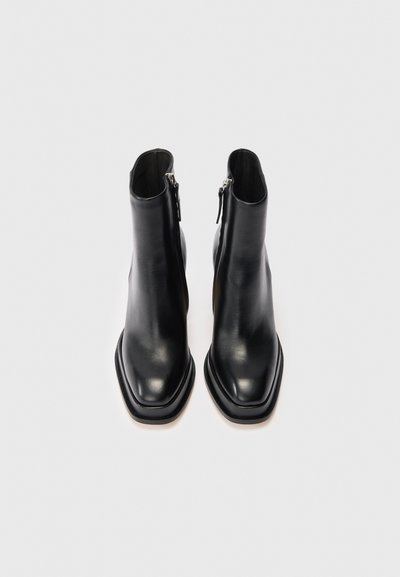Botas de cuero negras hasta el tobillo con una forma elegante, punta cuadrada y cierre de cremallera en la parte trasera. Textura suave con un diseño minimalista.