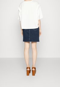 Bílý top s krátkým rukávem a volánovými detalemi na bocích, v kombinaci s tmavě modrou džínovou mini sukní a hnědými platformovými podpatky. Jednoduchý, moderní design.