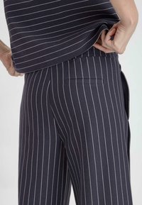 Navy raidalliset housut, jotka on valmistettu sileästä kankaasta. Housuissa on pystysuorat valkoiset raidat, joustava vyötärö ja takataskusuunnittelu.