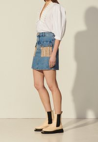 Jupe en denim avec poches plaquées en tissu à carreaux, associée à un chemisier blanc et des bottines beige avec des accents élastiques noirs et des semelles épaisses.