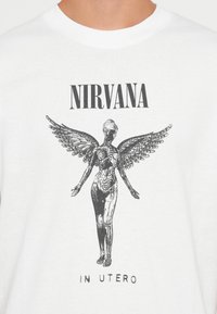 Biała koszulka z czarnym napisem "NIRVANA" u góry i "IN UTERO" na dole, z ilustracją skrzydlatej anatomicznej postaci kobiecej.
