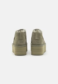 Olive zielone zamszowe botki za kostkę z podszewką z sztucznego futra, wyściełanym kołnierzem i płaską platformą. Logo UGG z tyłu.