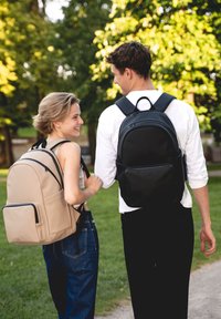 Két személy sétál egy parkban. Az egyikük bézs, sima tapintású hátizsákot visel; a másikuk fekete, cipzárakkal ellátott, elegáns hátizsákot.