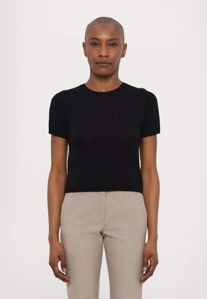 Musthave mustmærgiga lühikeste varrukatega kudumiga topp, millel on teemantmustrit, ümmargune kaelus ja liibuva siluettiga, millele on sobitatud heledat halli lõikega püksid.