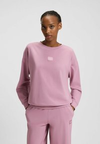 Felpa rosa con maniche lunghe,collo a giro e patch logo frontale. Realizzata in tessuto morbido con una vestibilità comoda. Abbinata a pantaloni coordinati.