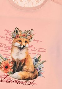 Helles rosa T-Shirt mit einer Fuchs-Illustration, die mit einer Blumenkrone geschmückt ist, umgeben von Blumen und stilisierten Text am unteren Rand.