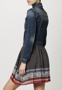 Jeansjacka i mörkblått, figurnära design med knappstängning och två sidofickor. Matchas med en mönstrad mörk klänning med spetsdetaljer.