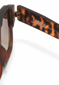 Brauner Schildpatt-Sonnenbrillenbügel mit Scharnier und weißem "JJXX Made in China"-Text auf weißem Hintergrund.