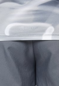 Pantalones cortos deportivos grises con tela texturizada y una sección superior de rayas claras. Presenta el logo "HEAT.RDY" a lo largo de la cinturilla.