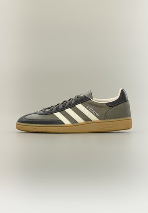 Baskets Adidas Spezial profil bas en gris foncé et noir avec des bandes blanches et une semelle en gomme, vue latérale sur fond neutre.