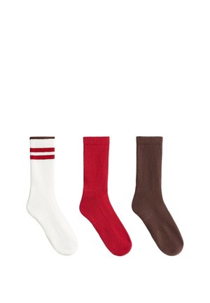 Trois chaussettes montantes côtelées en blanc avec des rayures rouges, rouge uni et marron uni, affichées côte à côte sur un fond blanc.