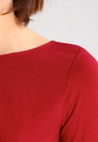 Rode, korte mouwen top met een gladde textuur en wijd decolleté, met zichtbare stiksels langs de schouder.