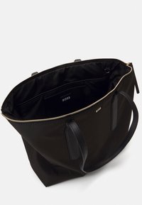 Černá taška přes rameno s hladkým textilním povrchem, koženými detaily a zlatým zipem. Interiér obsahuje logo značky a přihrádky pro organizaci.