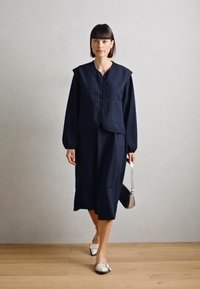 Marineblauw gestreepte wolvest met brede schouders, gecombineerd met een bijpassende midi-rok. Accessoires omvatten een kleine zilveren tas en platte schoenen.