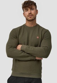 Sudadera verde oliva con superficie texturizada, cuello redondo y puños acanalados. Presenta un pequeño logo redondo en el pecho.