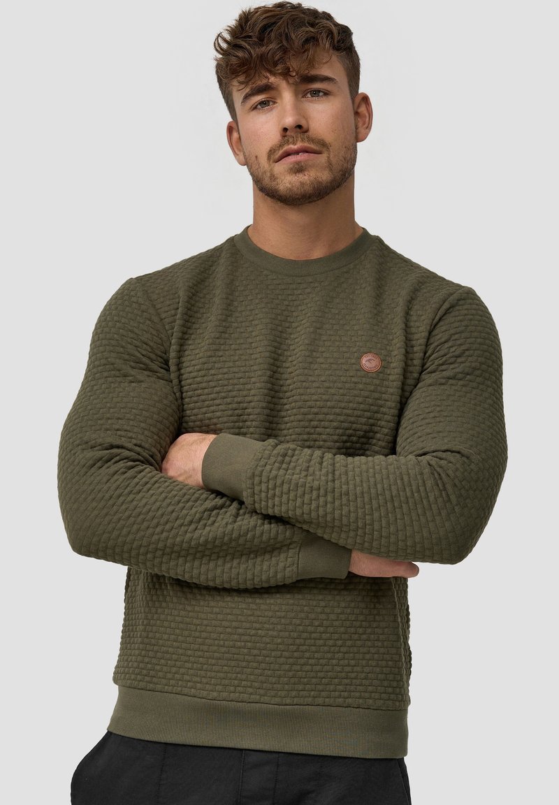 Sudadera verde oliva con superficie texturizada, cuello redondo y puños acanalados. Presenta un pequeño logo redondo en el pecho.