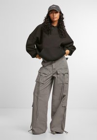 Felpa nera oversize con tasca frontale, abbinata a pantaloni cargo grigi larghi con diverse tasche e coulisse regolabili.
