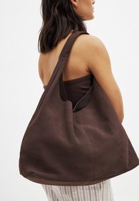 Brown suede tote bag with a large hobo shape, wide shoulder strap, and subtle stitching details. Open top design for easy access.