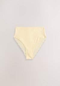 Lenjerie de damă galben deschis cu talie înaltă, cu dantelă festonată la deschiderile pentru picioare, așezată pe o suprafață neutră.