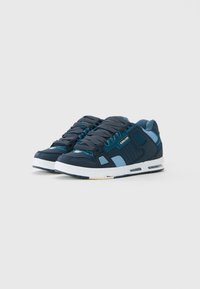 Tumed sinised ja helesinised sneakers valgete taldade ja mustade nööpidega helehallil taustal.