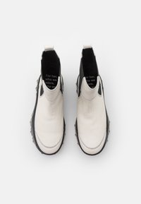 Botines de cuero blanco con paneles laterales elásticos negros, punta redonda y suela de goma texturada. El interior presenta texto impreso.