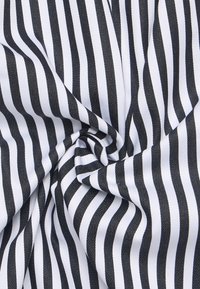 Tessuto di cotone con strisce alternate bianche e nere, piegato in modo compatto, mostrando una consistenza liscia e una leggera lucentezza dalla superficie tessuta.