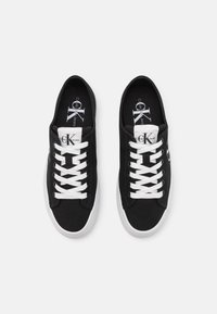 Czarne płócienne trampki z białymi sznurowadłami i podeszwą. Logo Calvin Klein po boku. Prosty design z okrągłym noskiem i płaską gumową podeszwą.