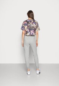 Haut floral court avec des motifs violets, roses et noirs associé à un pantalon de survêtement gris clair fuselé et des baskets blanches.
