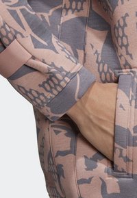 Růžová mikina s abstraktním šedým vzorem. Má žebrované manžety a boční kapsu, která zdůrazňuje měkkou, strukturovanou tkaninu.