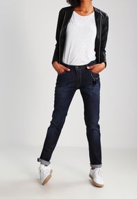 Mörka denimjeans med slim fit, kombinerat med en vit t-shirt och en svart läderjacka. Vita sneakers med bruna sulor. Enkel design utan mönster.