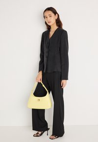 Čierne priliehavé sako s gombíkmi, v kombinácii s čiernymi nohavicami a čiernymi sandálmi na podpätku so remienkami. Drží žltú kabelku s oblým tvarom a kruhovým detailom.