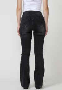 Črne flare jeans hlače z visokim pasom, ki imajo zadnje žepe z dekorativnim šivanjem in gladko denim teksturo.