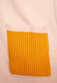 Stickad tröja med en mjuk rosa botten och en stor ribbad ficka i senapsgul färg med horisontella ränder upptill.