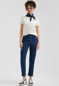 Bela majica s kratkimi rokavi, mornarsko modra ruta za vrat, temno modri jeans in črno-bele teniske. Ohlapen outfit s preprostim oblikovanjem.