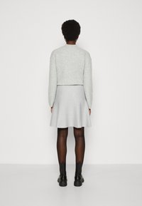 Grijze geribbelde cropped trui en lichtgrijze uitlopende rok, gecombineerd met zwarte enkellaarsjes en doorschijnende zwarte panty. Effen achtergrond.