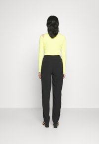 Pitkähihaineonkelvaväri toppi avokainalalla, yhdistetty mustiin säädettäviiin housuihin, joissa on takataskut, ja mustat block-korkokengät.