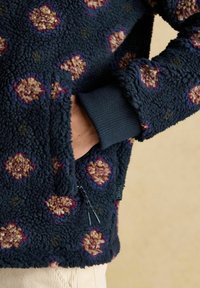 Blaue Fleecejacke mit floralem Muster, mit Reißverschlusstaschen und gerippten Bündchen. Weicher Stoff und lässige Passform, mit kontrastierenden floralen Akzenten.