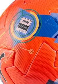 Balón de fútbol con certificación FIFA Quality Pro, color naranja brillante con superficie texturizada, detalles en azul y una etiqueta con logotipos y un código numérico.