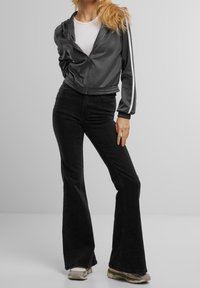 Gray cropped zip-up jacket with white side stripes, paired with black flared jeans and light-colored sneakers. Smooth texture, casual design.