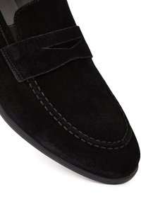 Mocassins en suède noir avec un design couturé, une bande décorative à l'avant et une semelle en caoutchouc lisse. Texture douce et forme classique.