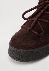 Baskets montantes en suedine marron avec semelle en caoutchouc noir texturé, présentant un design à lacets épais et un bout arrondi.
