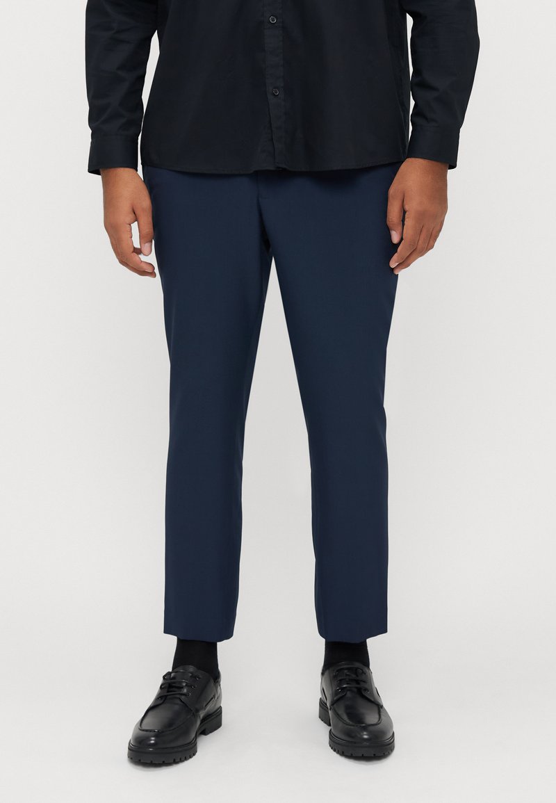 Marineblaue Hose mit maßgeschneiderter Passform, gefertigt aus glattem Stoff. Kombiniert mit einem schwarzen Hemd und schwarzen Schuhen, mit einem einfachen, eleganten Design.