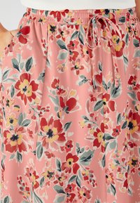 Falda floral de suave tela rosa claro con vibrantes patrones de flores rojas, amarillas y verdes. Cintura elástica con un detalle de cordón.