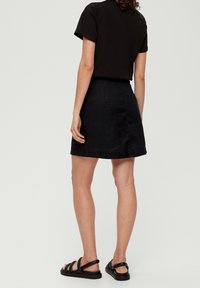Jupe en lin noire avec une taille cintrée et un ourlet évasé. Assortie à un haut noir à manches courtes et des sandales plates noires. Design simple, sans motifs.